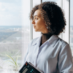 Mulher adulta olhando pela janela com expressão confiante e serena, representando a reconstrução da autoconfiança após desafios profissionais.